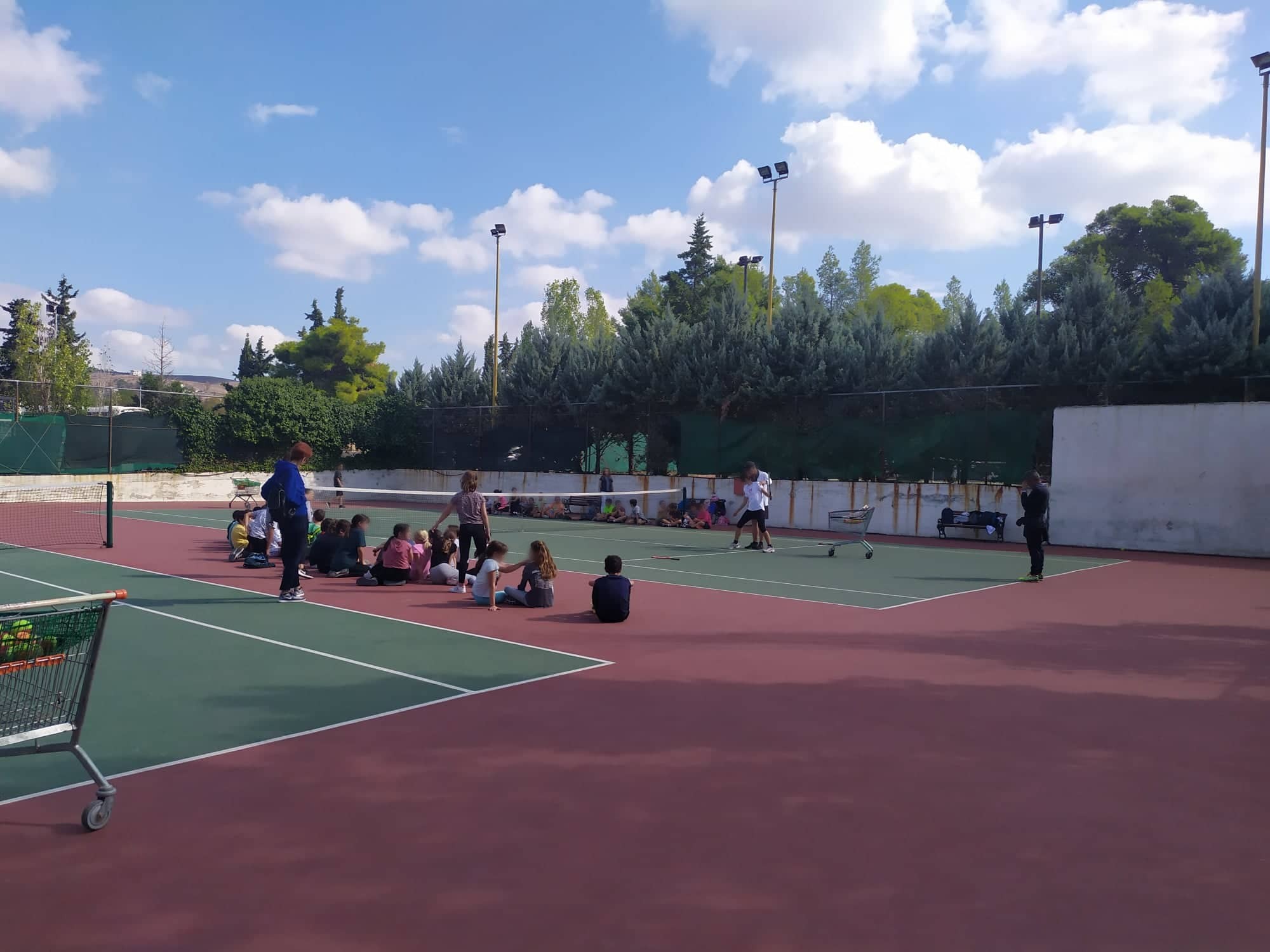 Οι μαθητές ασκούνται στο γήπεδο τένις με την καθοδήγηση των προπονητών.